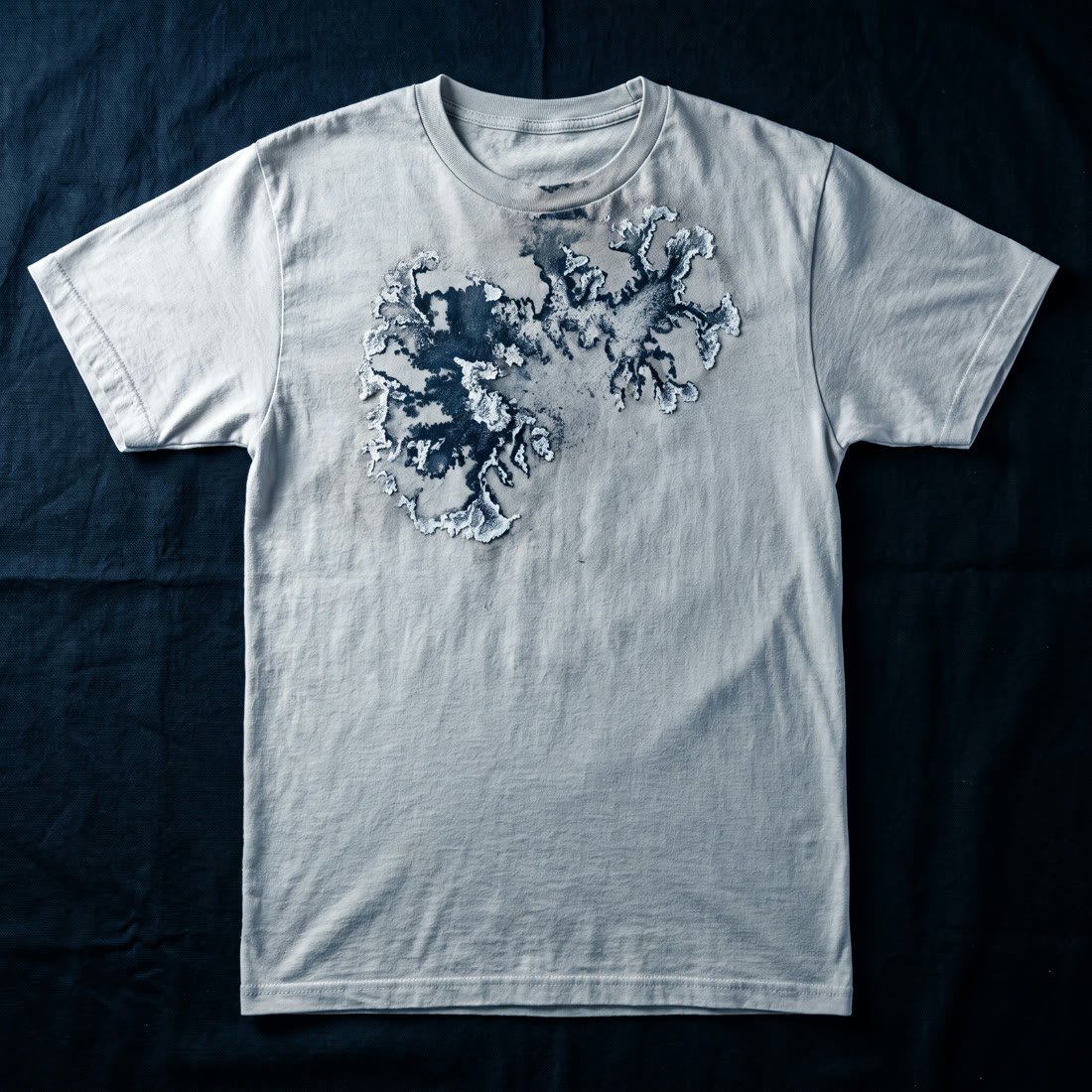 Drop 003, Salt: the same shirt carrying a field of ink eaten away by salt into branching edges, crusted pale at the boundaries.